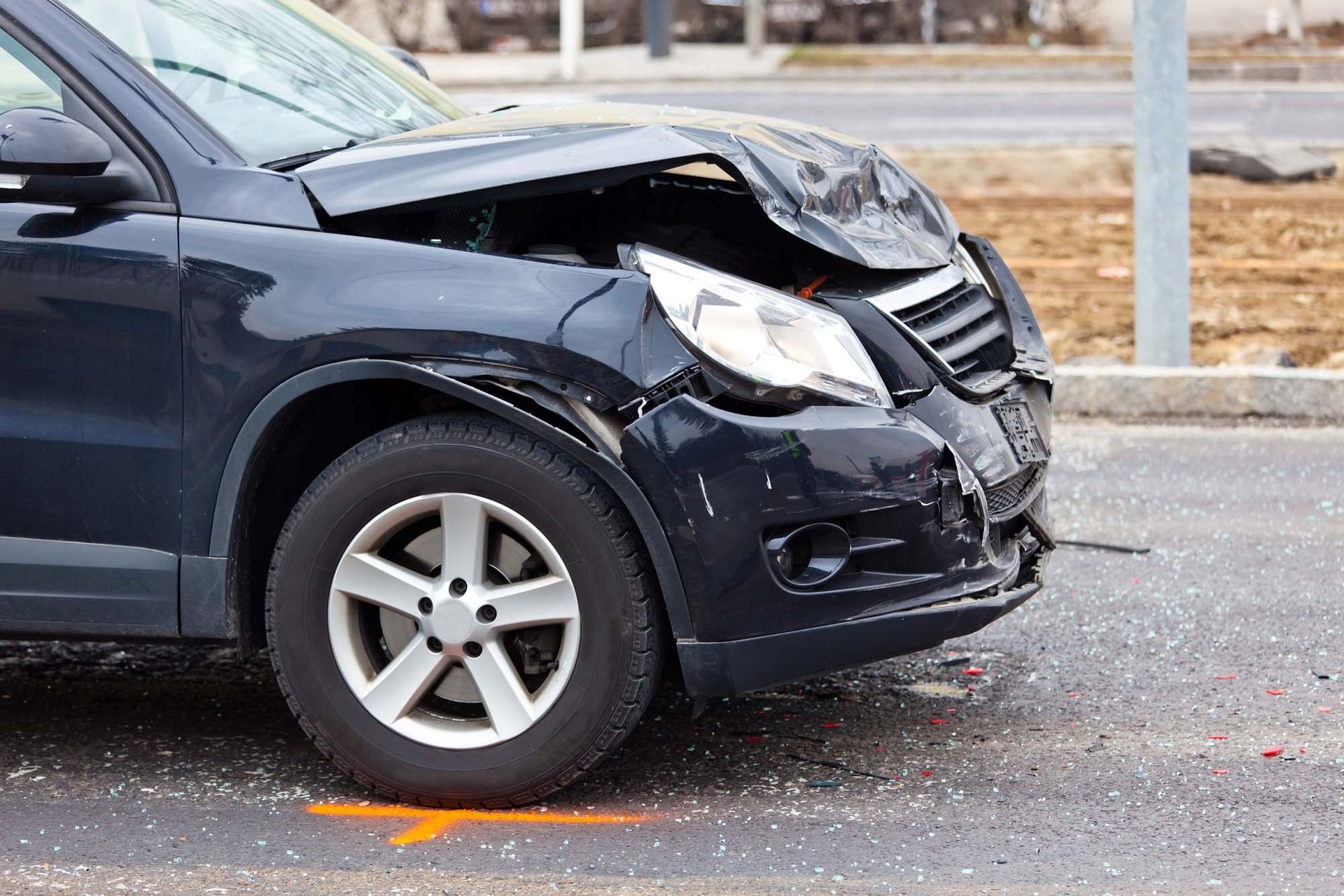 A black car with a damaged front end is parked on the side of the road.