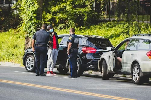 Police officers stand by two cars stopped on a roadside after a crash.