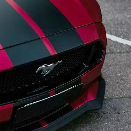 Red and black Ford Mustang with racing stripes, close-up of front grill and emblem.