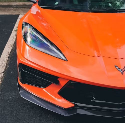 Bright orange sports car front corner with sharp headlight and black grille parked on pavement