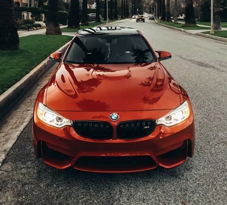 Bright orange BMW sports car parked on a tree-lined street.