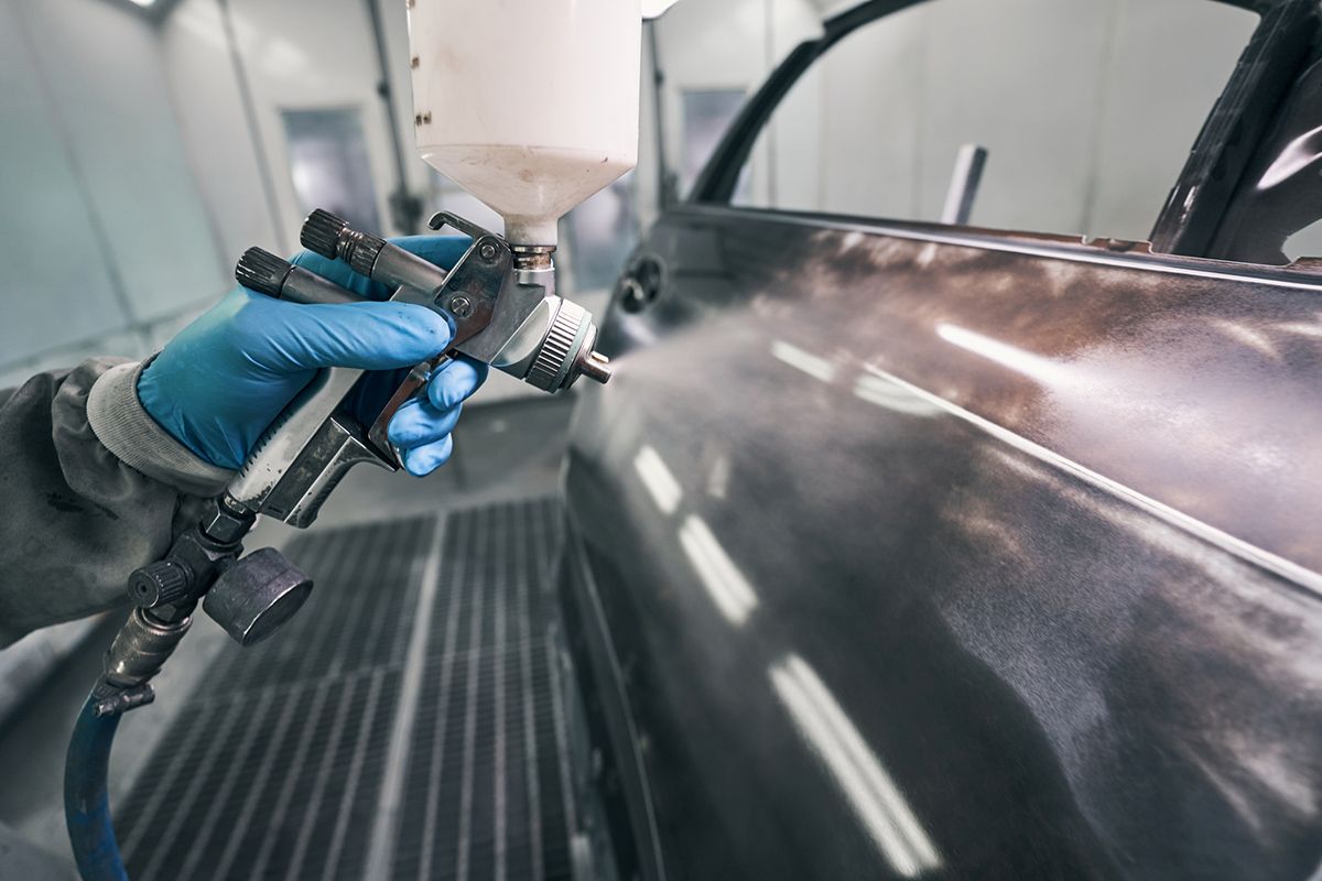 A person is spraying paint on a car door in a garage.