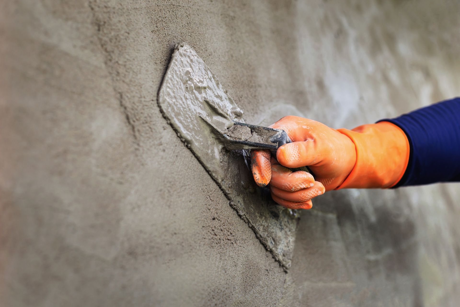 Gloved hand smoothing wet concrete on a wall surface with a trowel.