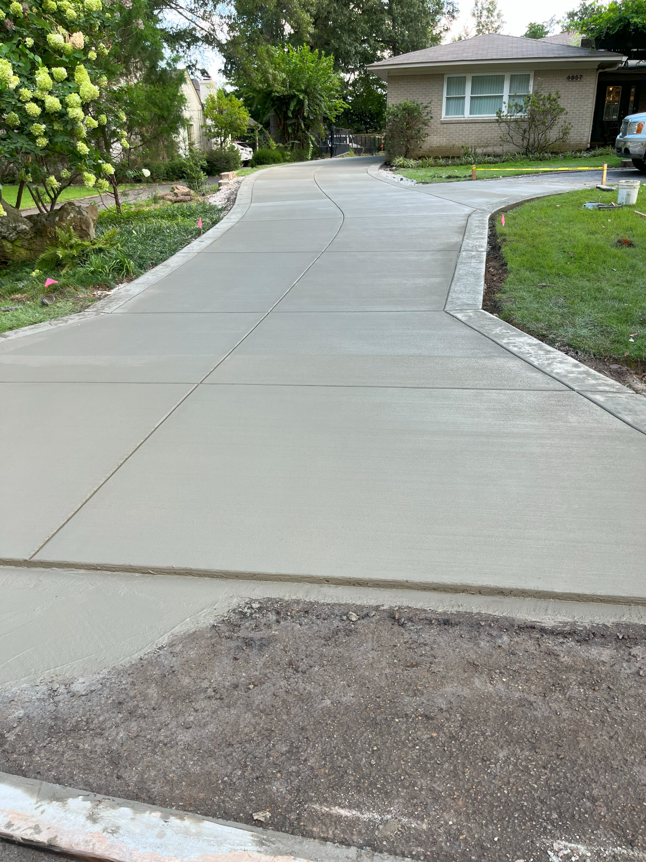 New concrete driveway leading to a house, bordered by grass and greenery.