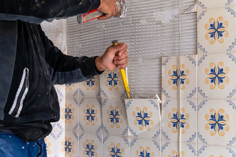 Person using a chisel to remove patterned tiles from a wall.