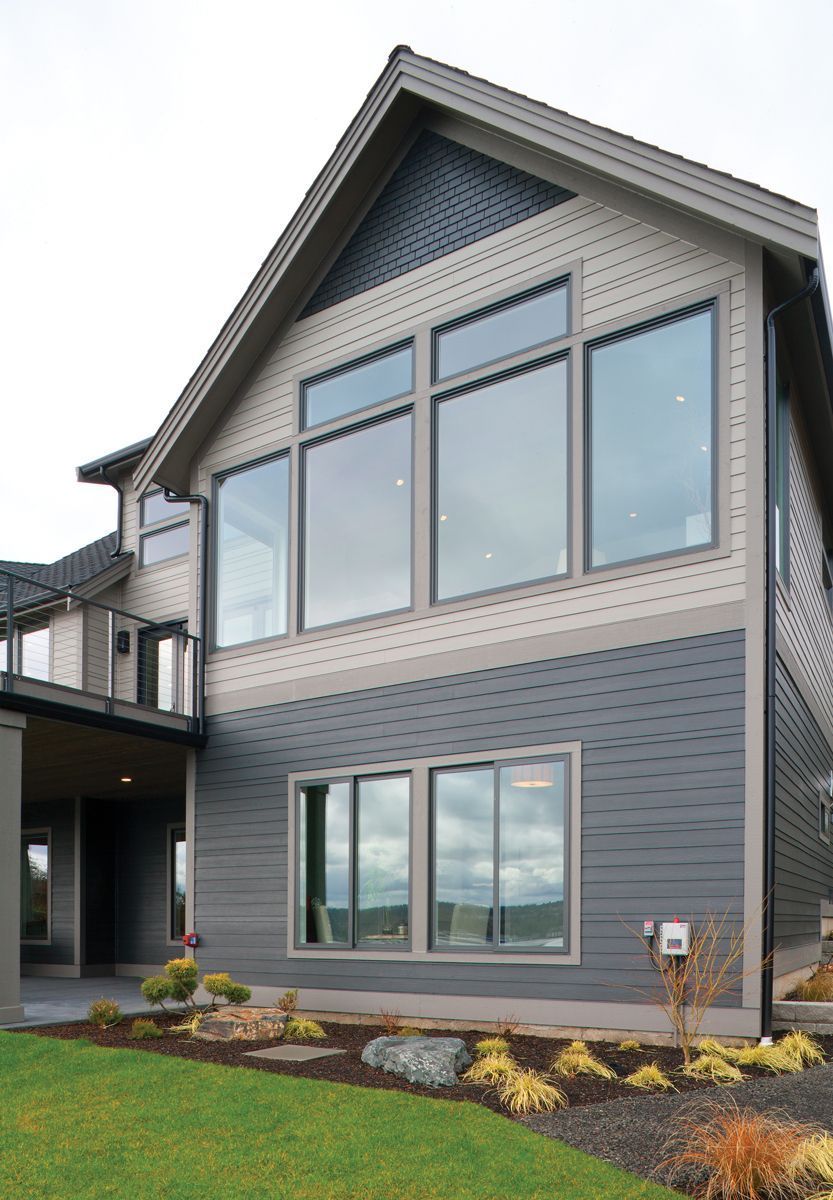 A two-story house with dark gray horizontal siding on the lower level, light beige siding above, and large windows.
