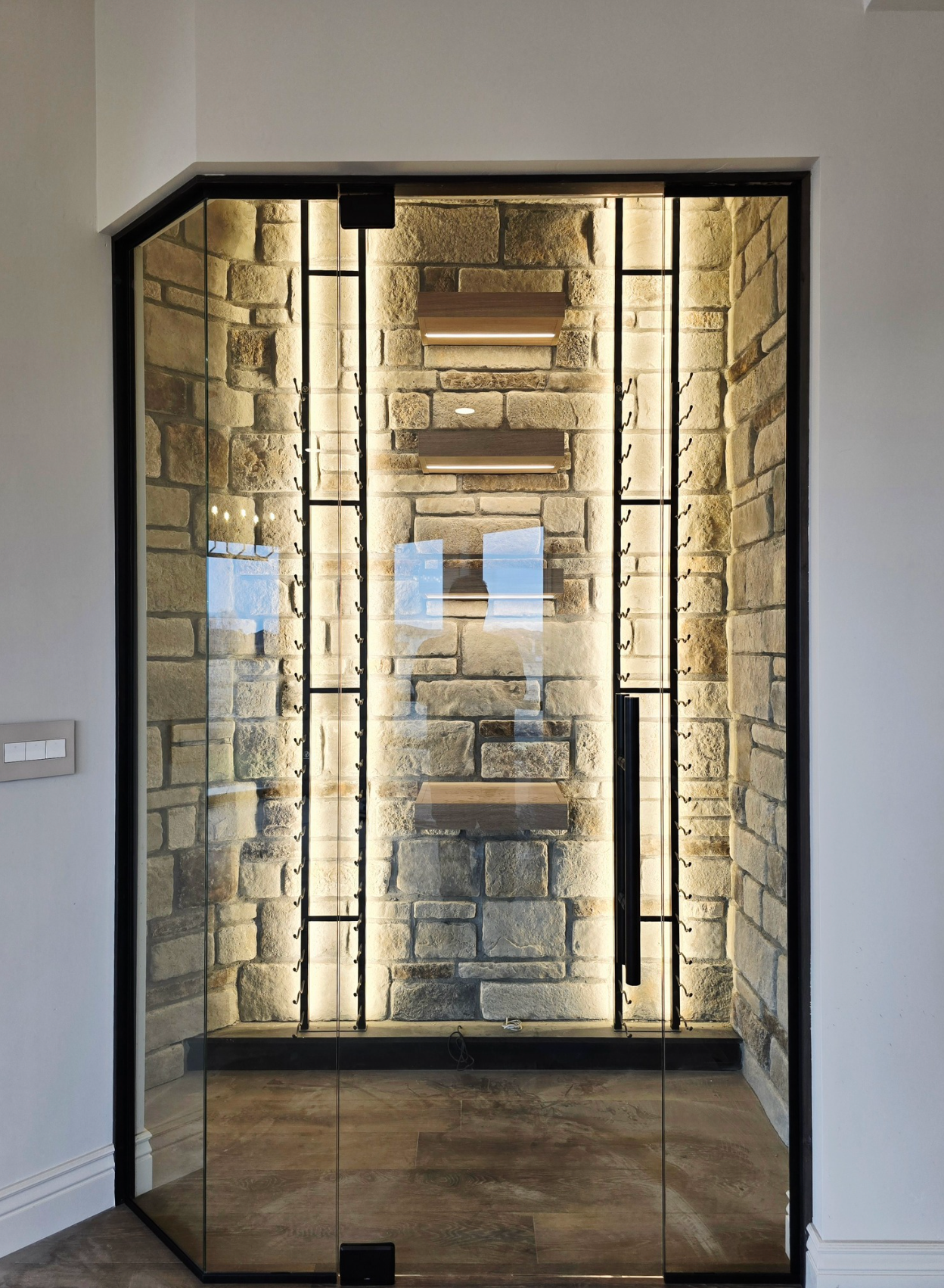 Wine cellar with glass door, stone walls, and interior lighting.