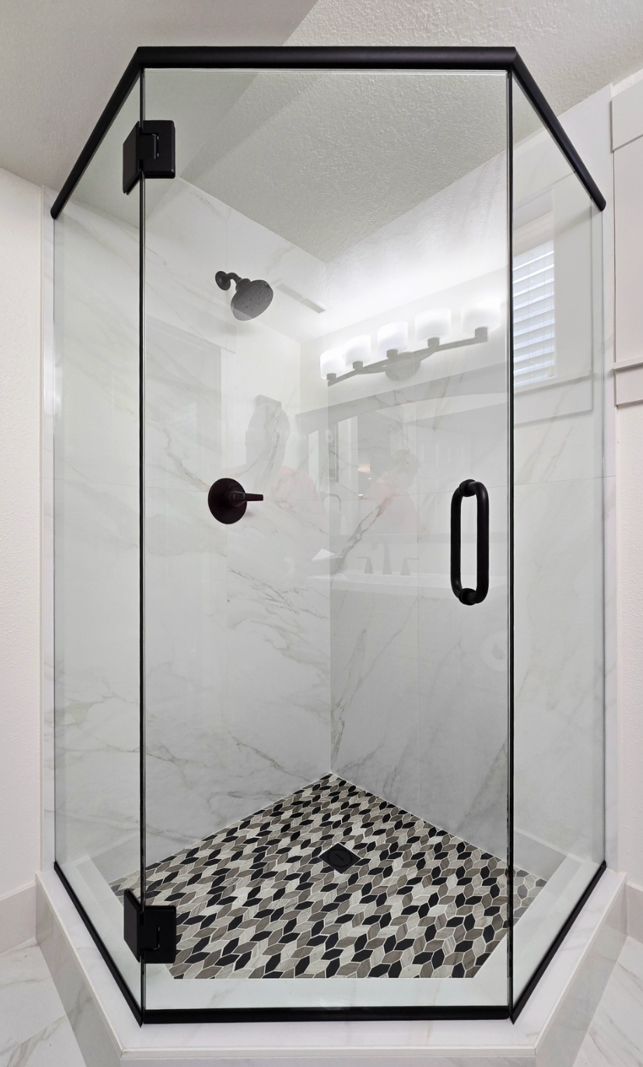 A modern corner shower with clear glass walls, black trim, and a patterned mosaic floor.