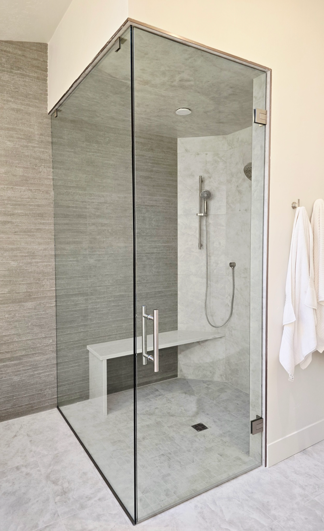 Glass-enclosed shower with a built-in bench. Gray tile interior, chrome fixtures, and glass door. 