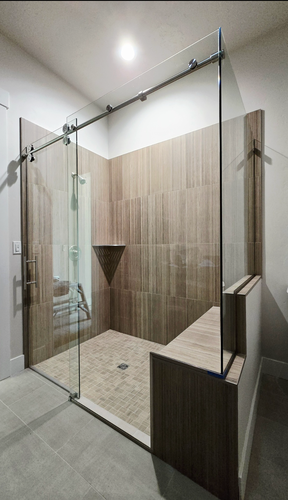 Modern shower with glass doors, wood-look tile, and a built-in bench. Neutral colors dominate.