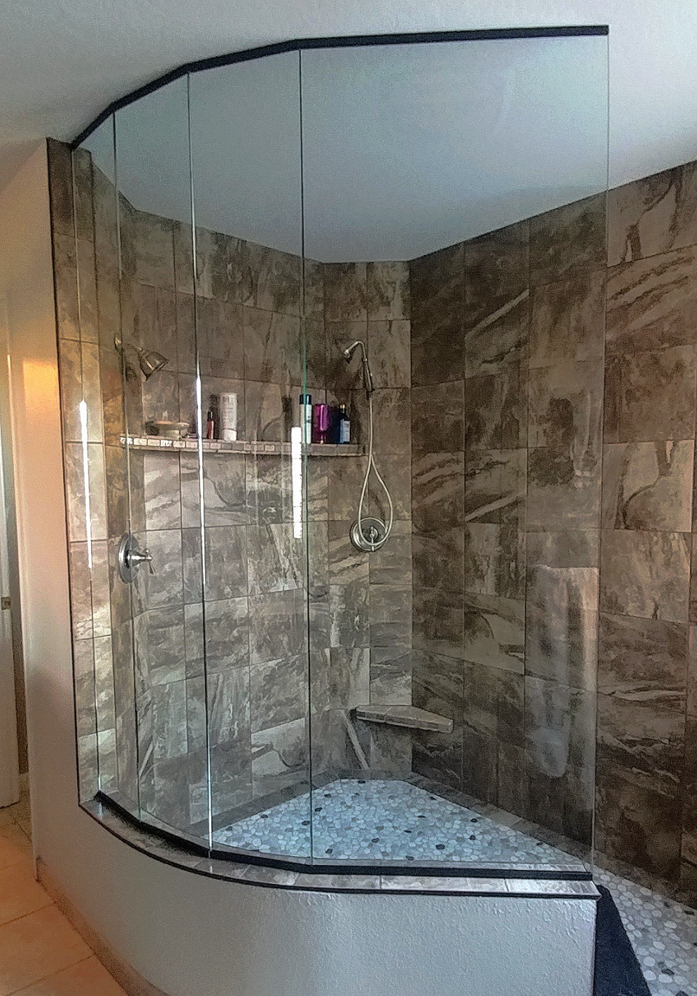Shower with curved glass enclosure and tiled walls.