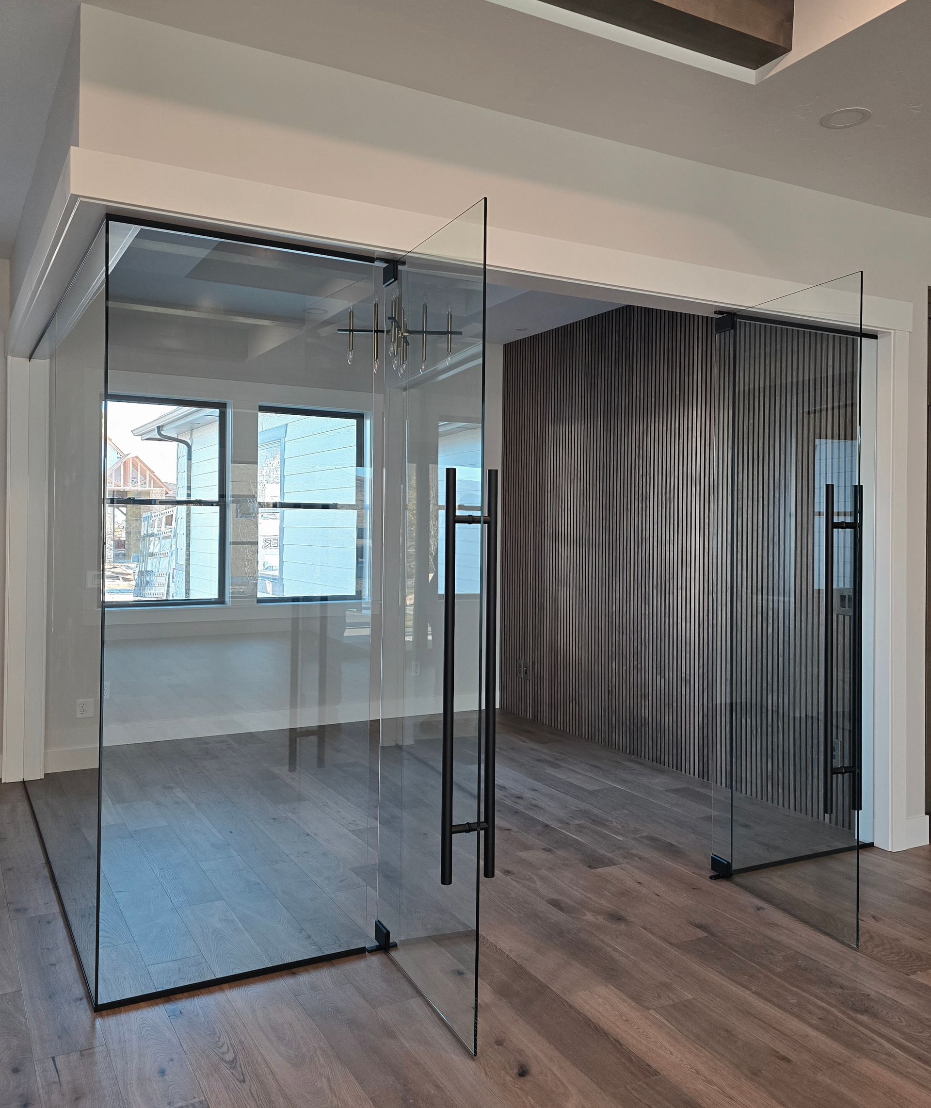 A glass-walled office entry featuring tall black handles, wood flooring, and a decorative ribbed feature wall.