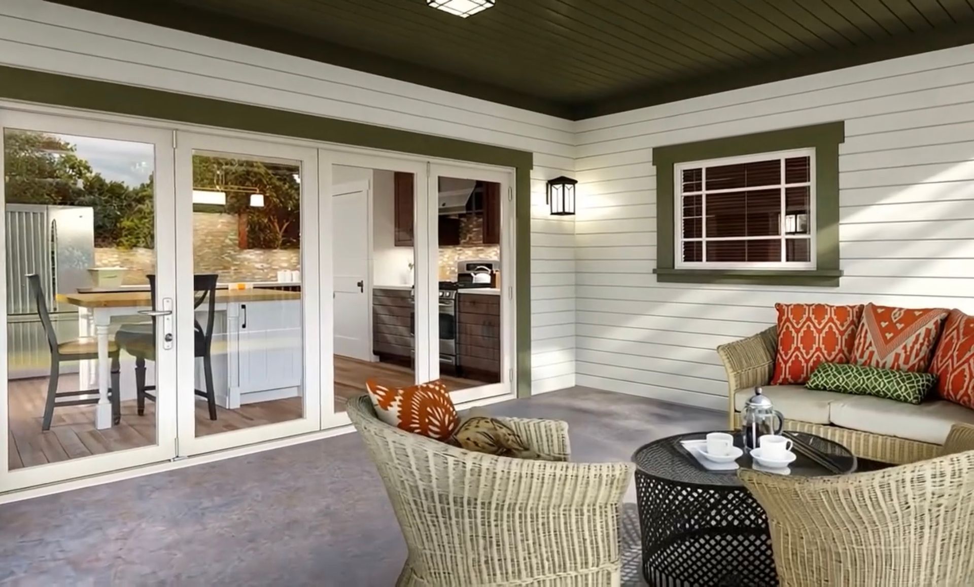 A covered outdoor patio featuring a wicker furniture set, white siding, olive green trim, and sliding glass doors.