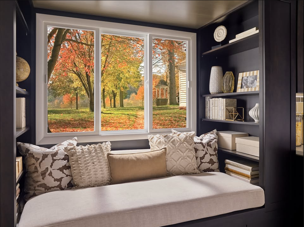 Cozy reading nook with window seat, dark shelves, and autumn trees outside large windows
