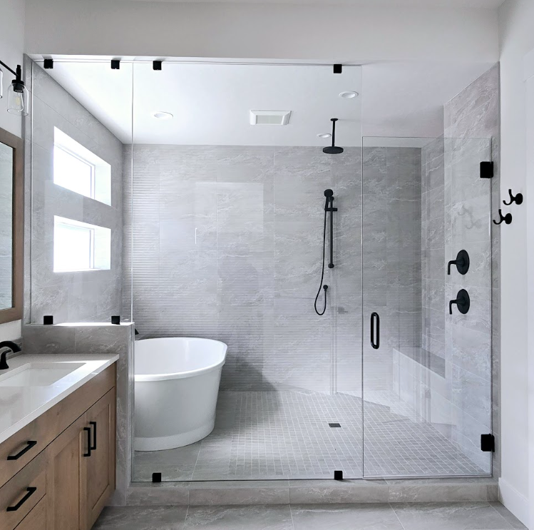 Modern bathroom with glass shower enclosure, freestanding tub, and light gray tile walls