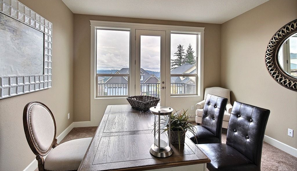 A dining room featuring a wooden table, two dark leather chairs, one light upholstered chair, and windows with a view.