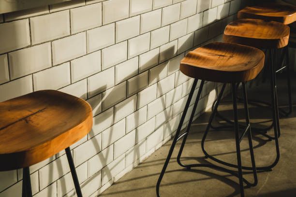 Wooden bar stools with black legs against a white tile wall.
