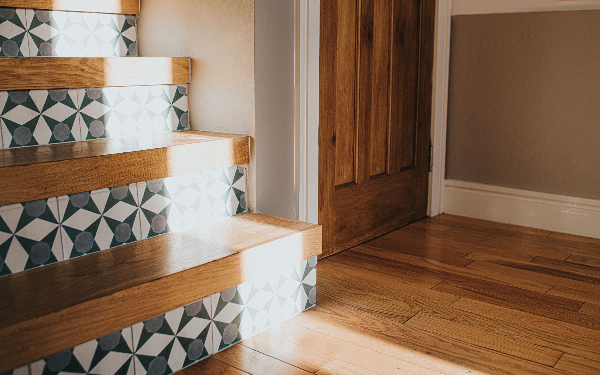 Wooden staircase with patterned tile risers, sunlight, and wooden door.