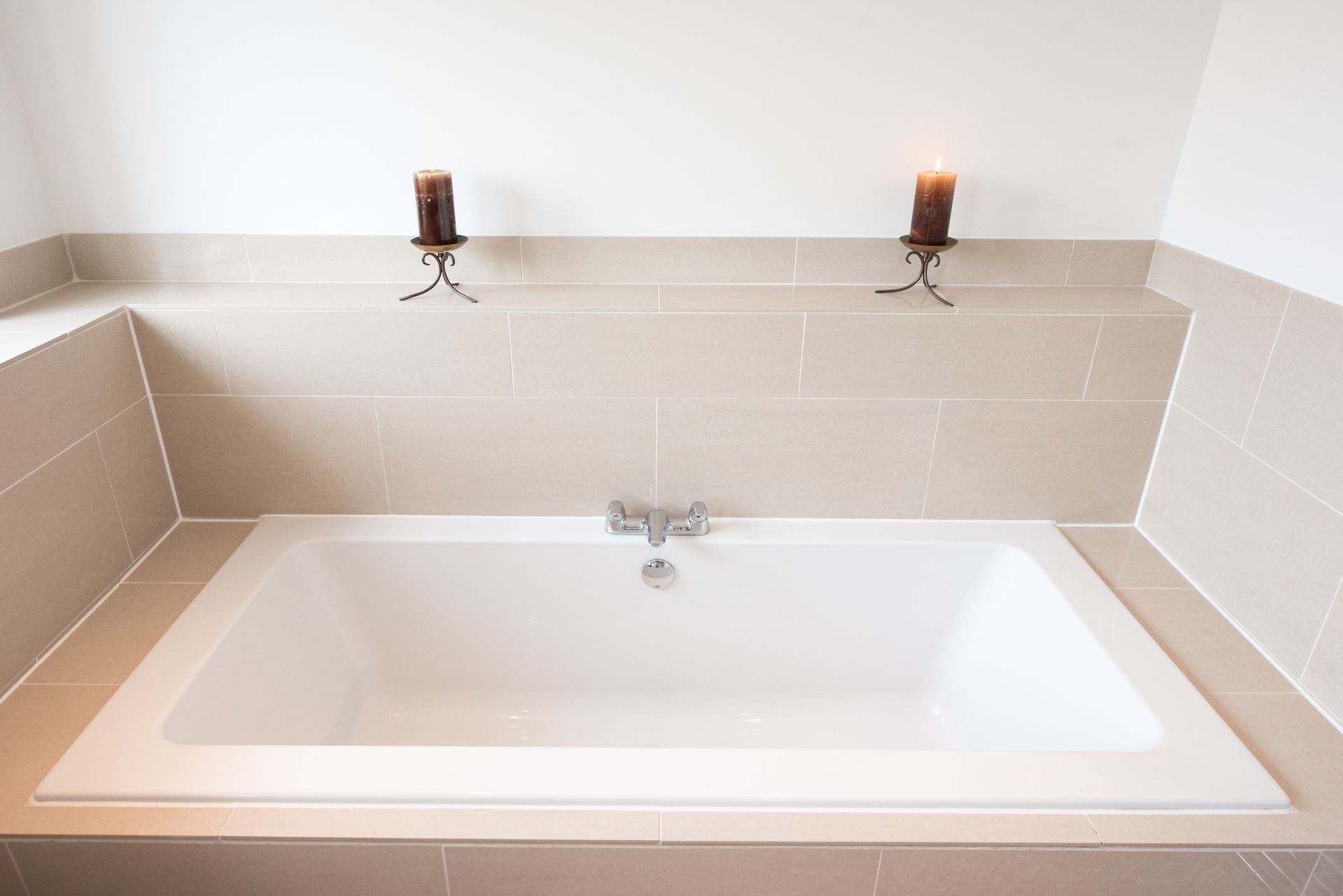 White bathtub set in a tiled alcove, with two candle holders mounted above. White bathtub set in a tiled alcove, with two candle holders mounted above.