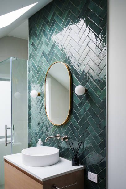 Emerald green herringbone tile bathroom wall with oval mirror, white sink, and sconces.