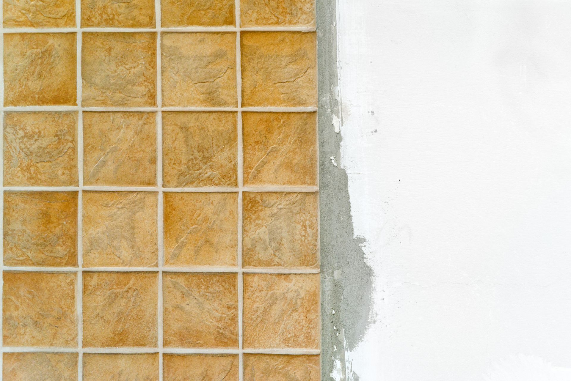 Tile installation in progress: Brown square tiles adjacent to unfinished white wall. Tile installation in progress: Brown square tiles adjacent to unfinished white wall.