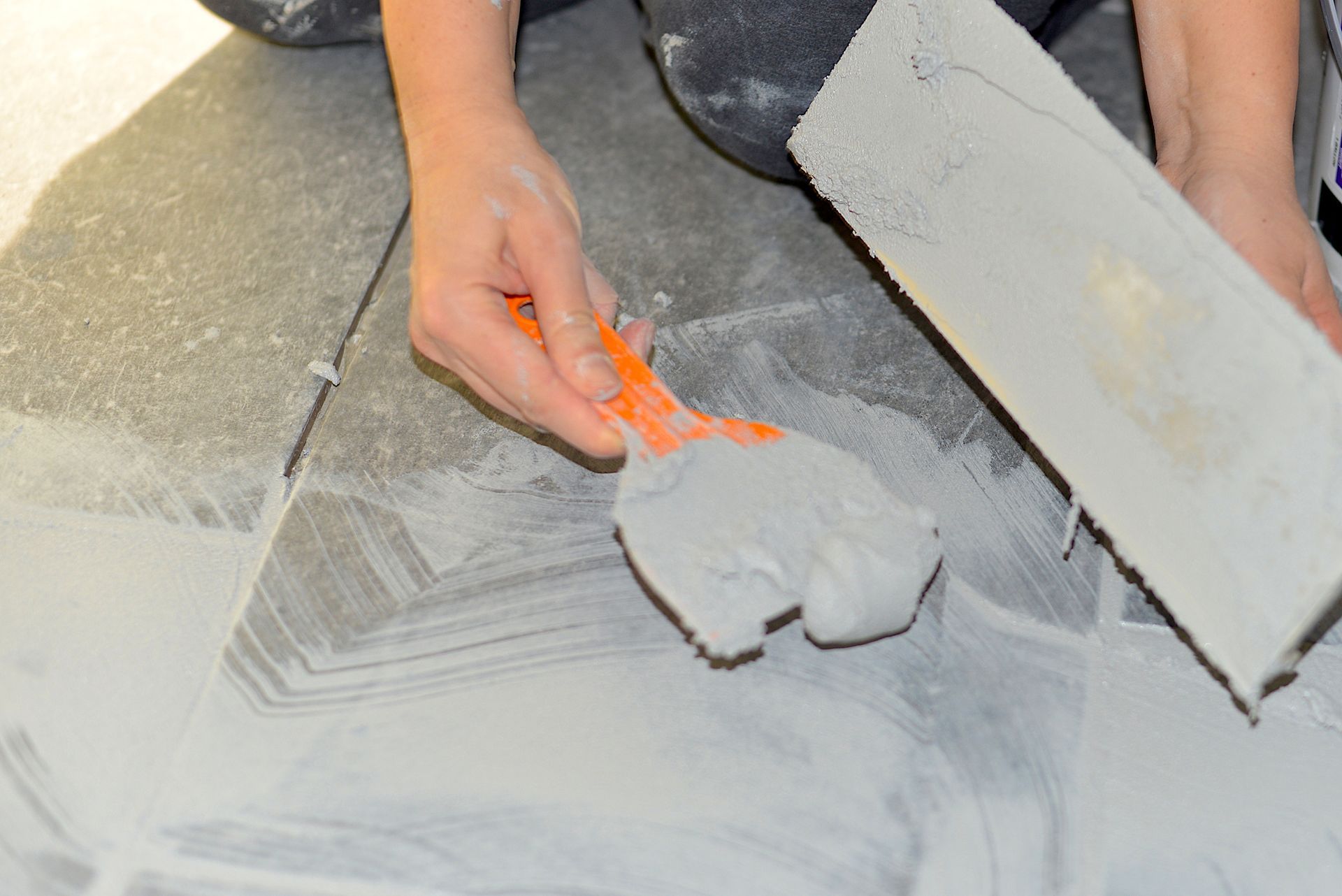 Person using a trowel and grout spreader to apply grout to floor tiles. Person using a trowel and grout spreader to apply grout to floor tiles.