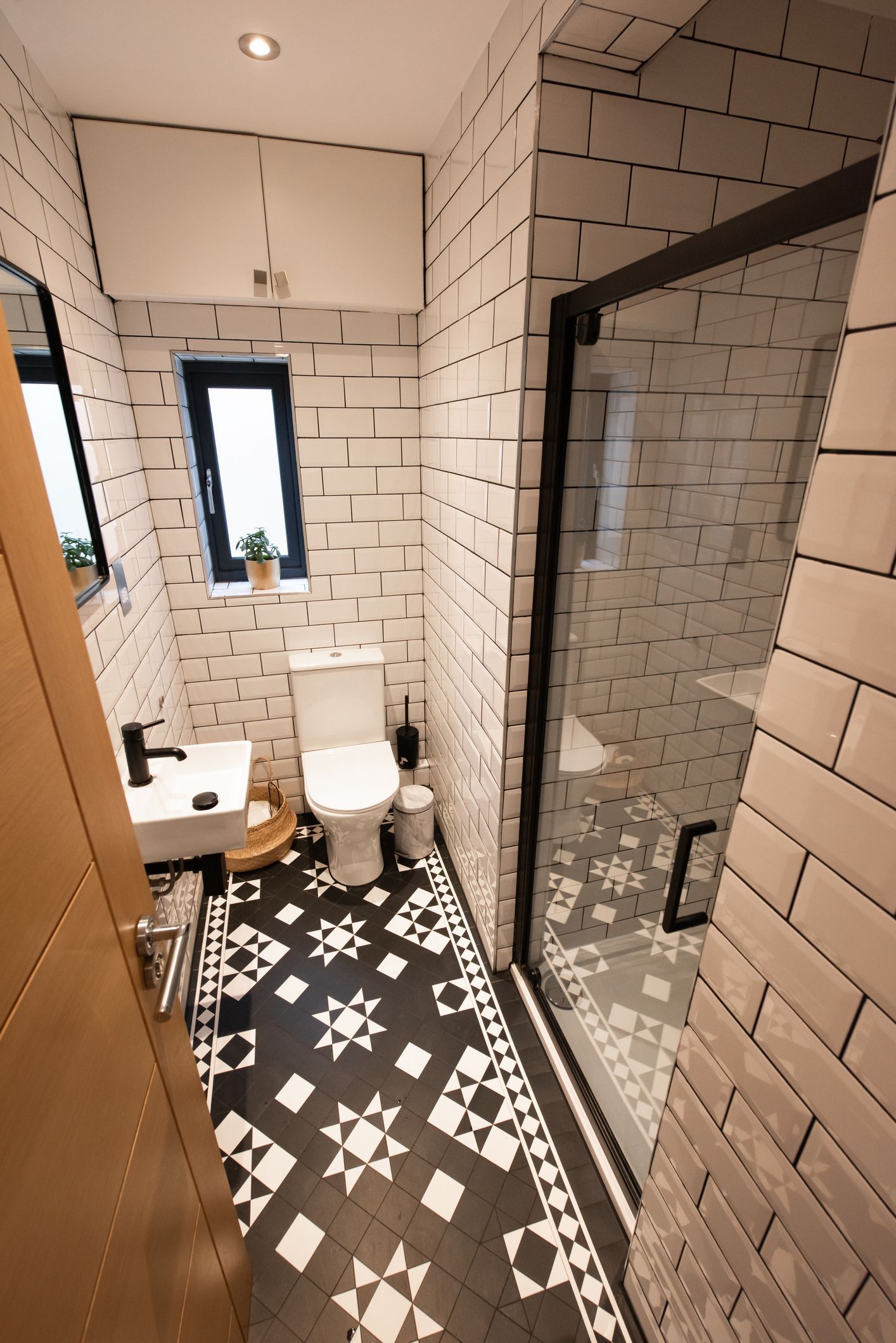 Small bathroom with black and white patterned floor, white brick-like tiles, toilet, and glass shower door. Small bathroom with black and white patterned floor, white brick-like tiles, toilet, and glass shower door.