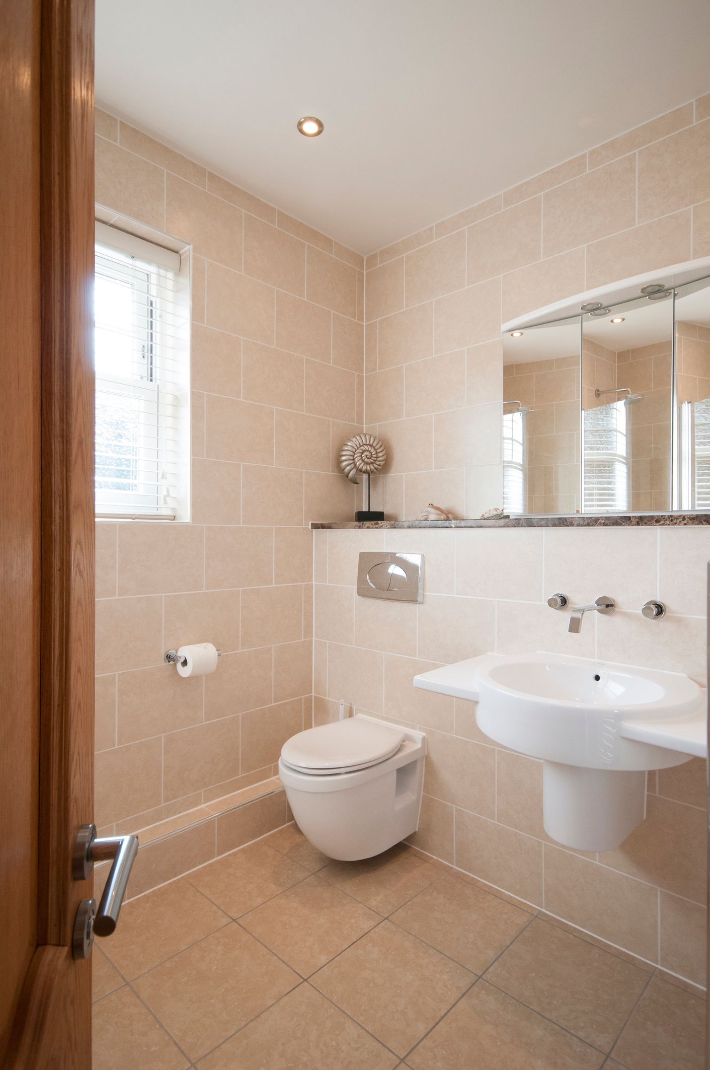 Bathroom with beige tiled walls, white fixtures, and a window with blinds. Bathroom with beige tiled walls, white fixtures, and a window with blinds.