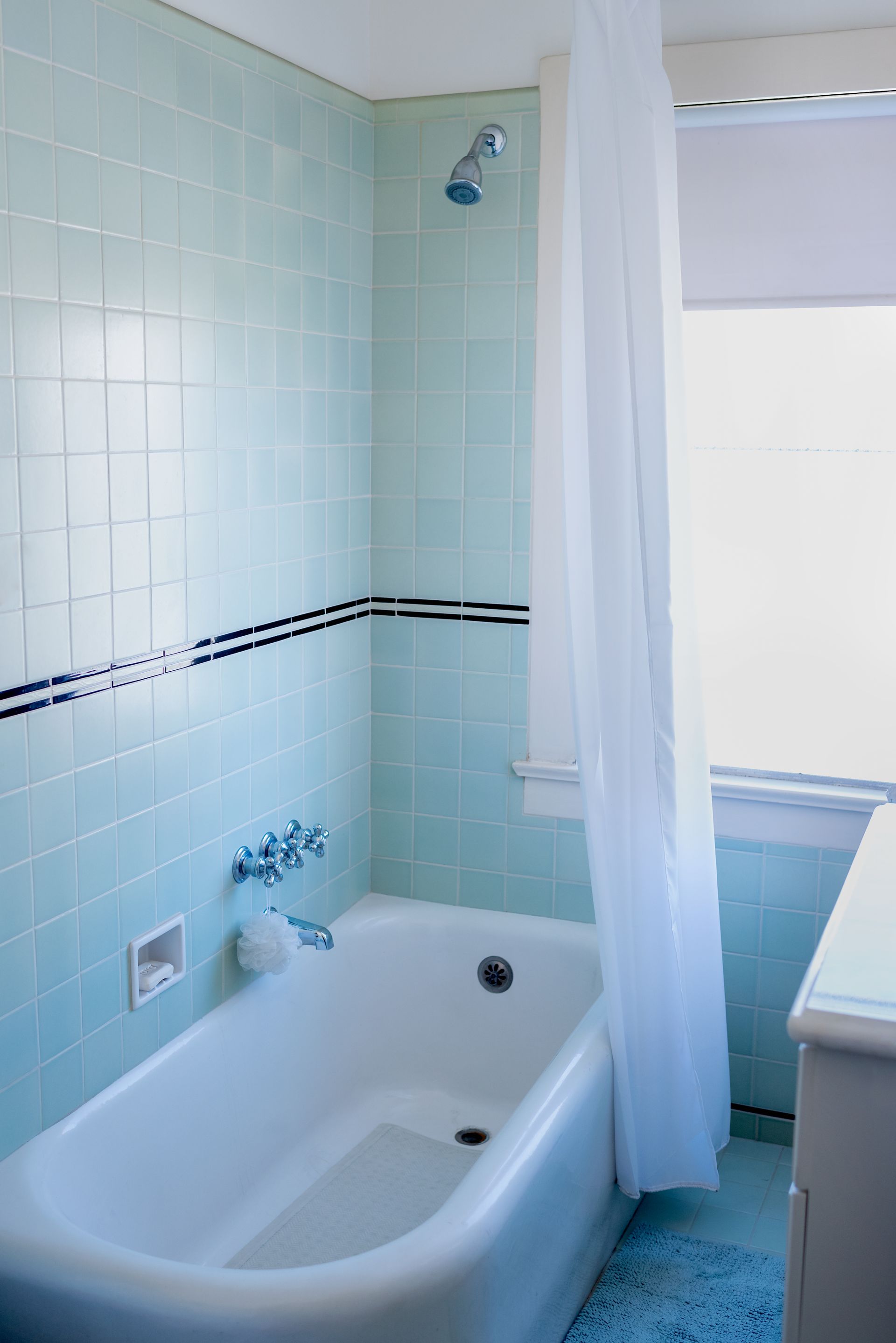 Light blue tiled bathroom with a white bathtub and shower curtain.