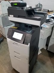 Office copier and printer machine in a workspace, with a touchscreen control panel and paper trays.