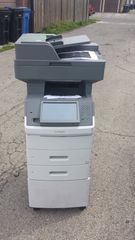 Gray office copier standing on a gravel path outdoors, with its front panel open.