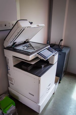 Office copier/scanner with open lid and control panel beside a wall in a small room