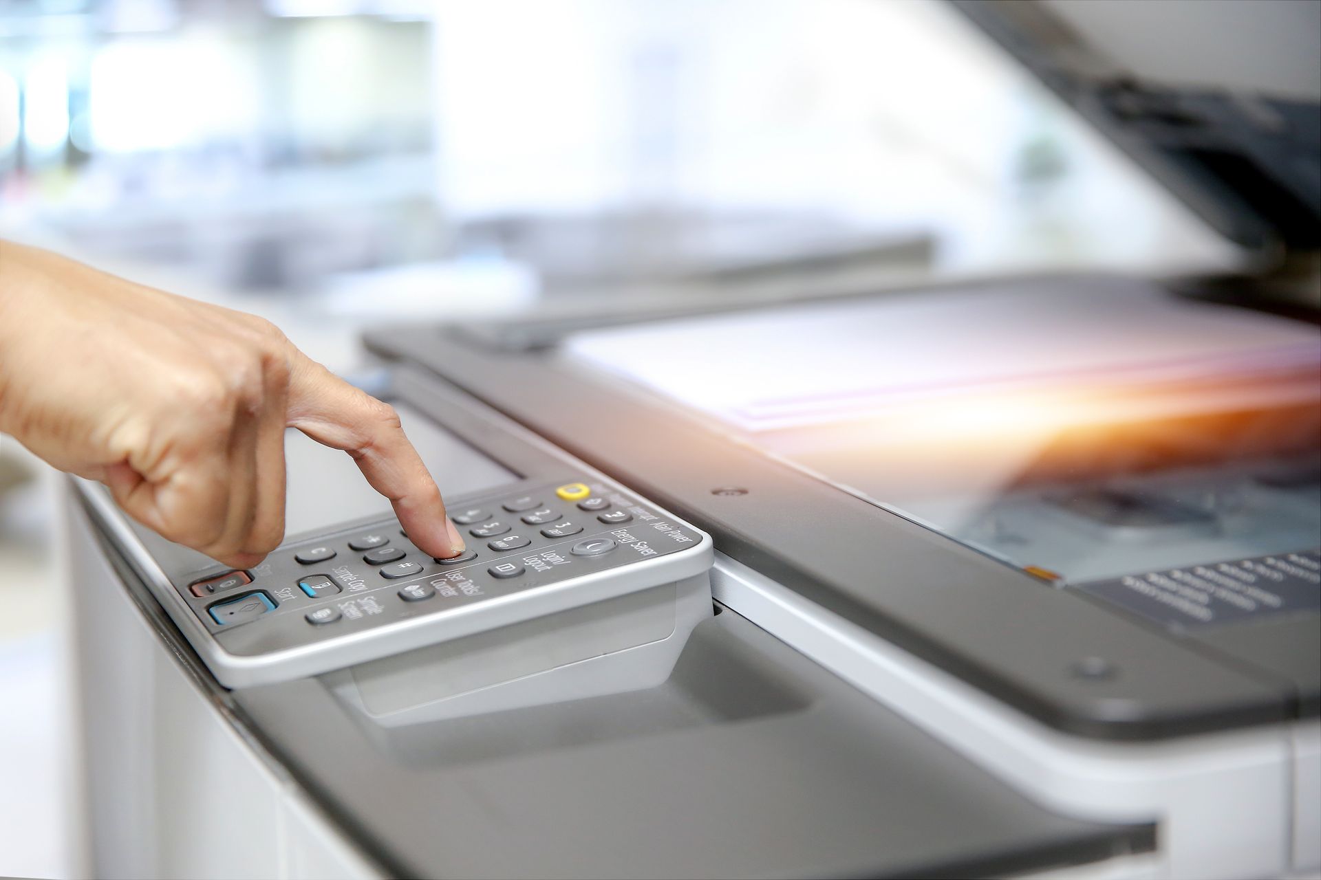 Hand pressing a calculator on a copier scanner bed in an office setting