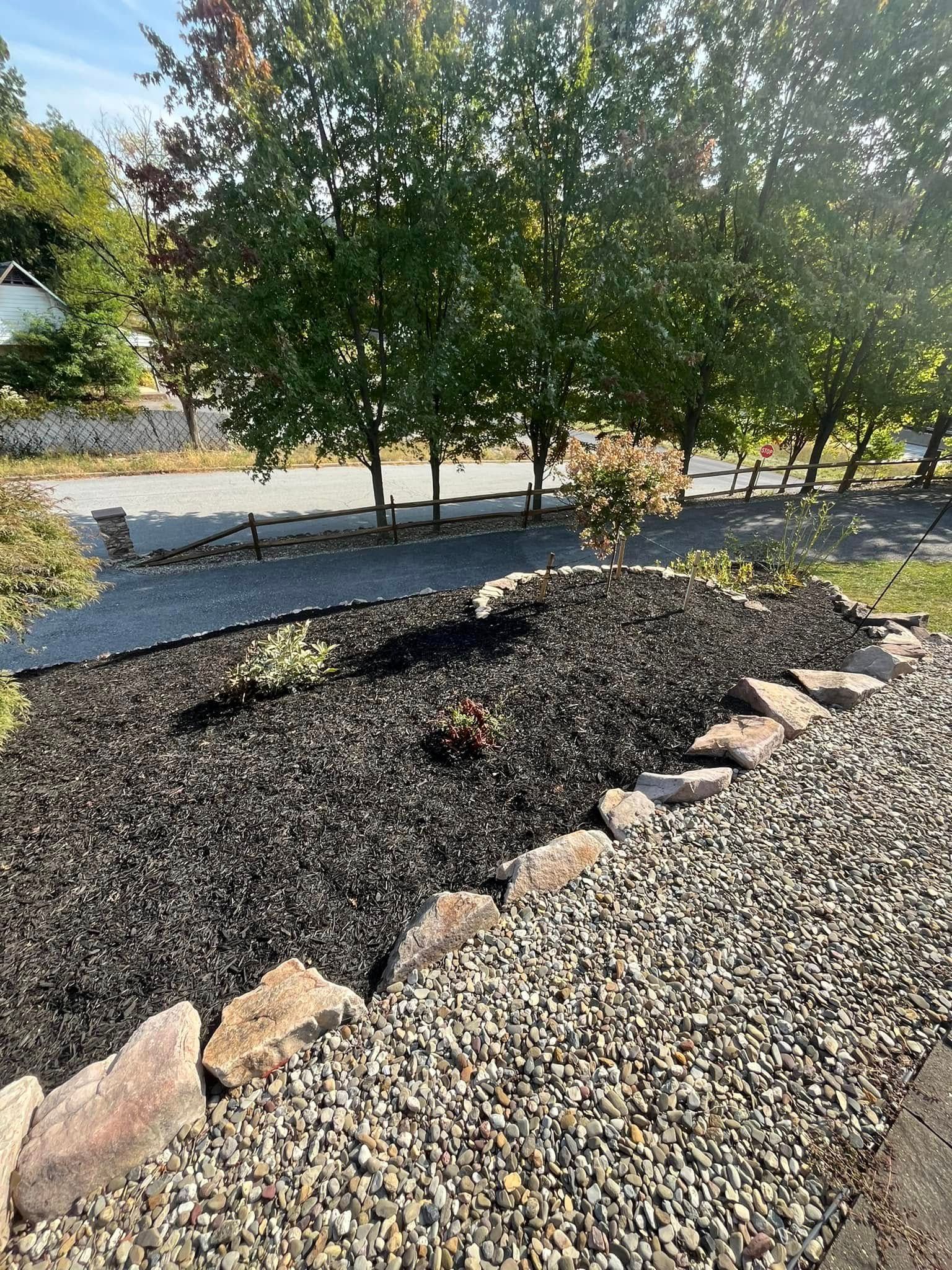 A pile of gravel and rocks in a yard with trees in the background.