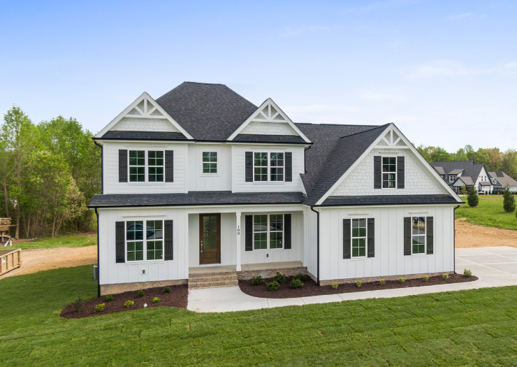 A large white house with black shutters is sitting on top of a lush green field.