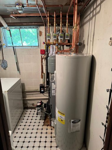 Basement utility room with water heater, furnace, exposed pipes, and a small window.
