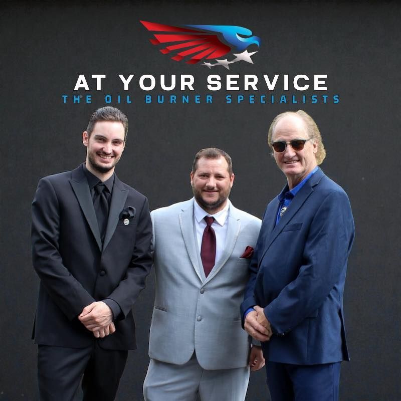 Three men in suits standing before a sign reading “At Your Service” and “The Oil Burner Specialists.”