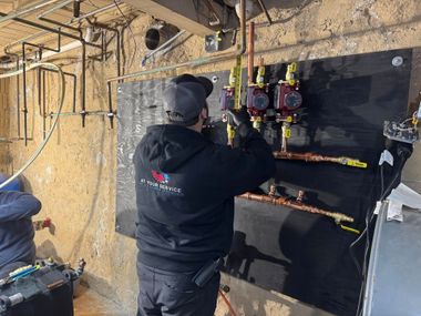 Worker installing wiring on a black electrical panel in an unfinished room