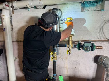 Worker in black shirt adjusts a yellow valve on a pipe in a utility room.