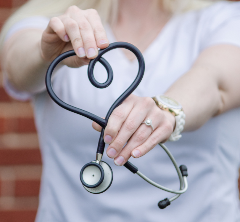 A woman is holding a stethoscope in the shape of a heart