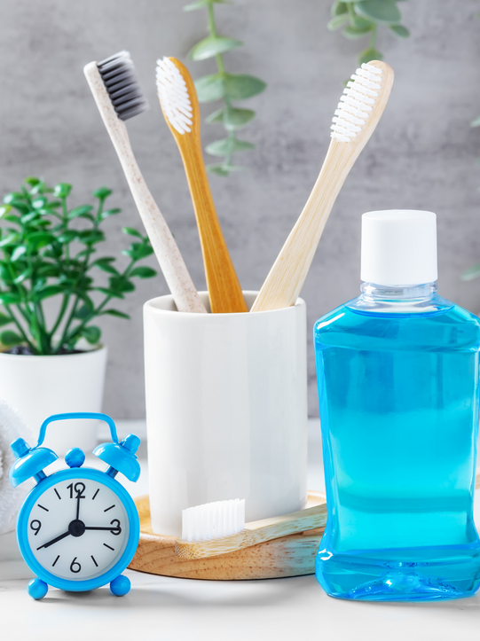 A bottle of mouthwash , toothbrushes , and an alarm clock on a table.