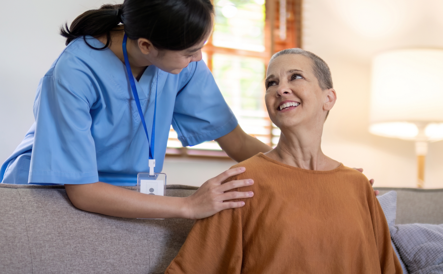 A nurse is talking to an elderly woman who is sitting on a couch.
