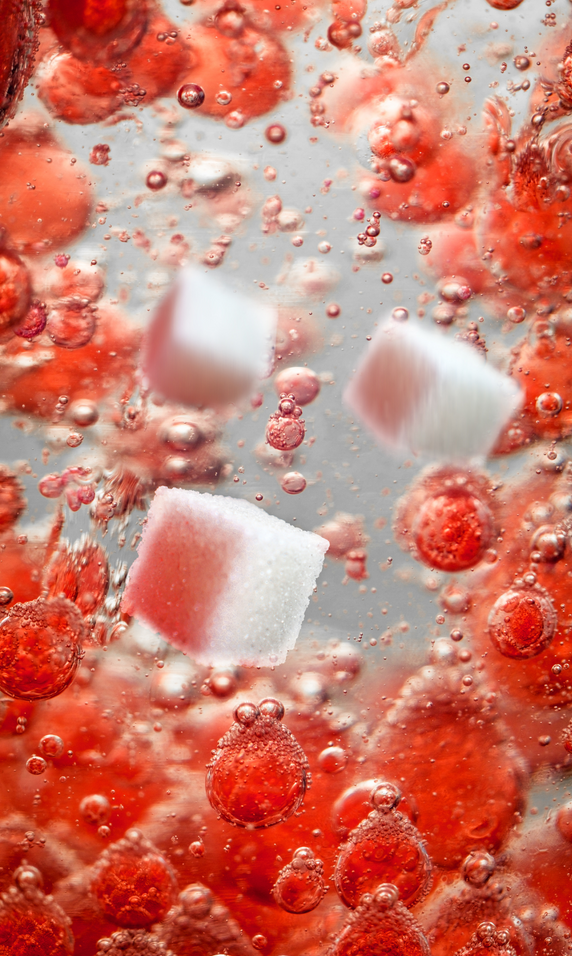Sugar cubes are falling into a red liquid with bubbles.