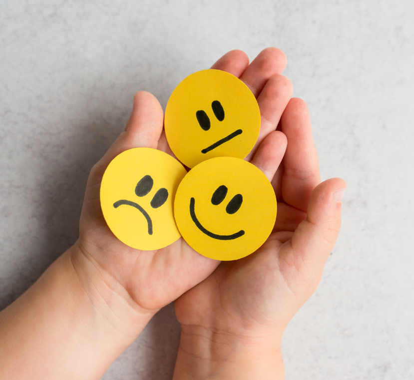 A child is holding three yellow smiley faces in their hands