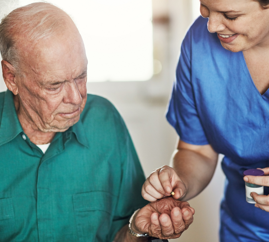 A nurse is giving an elderly man a pill.