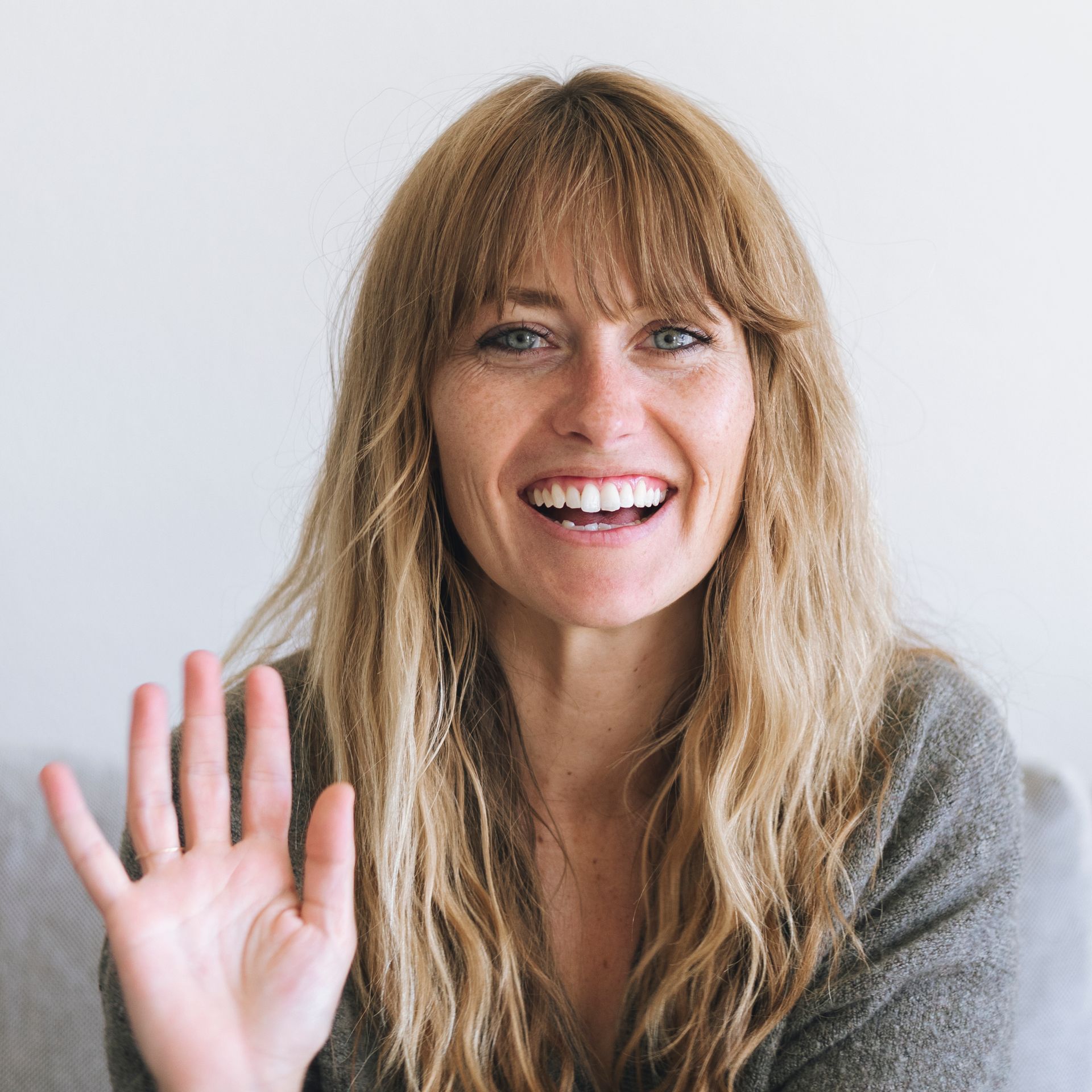 A woman wearing glasses is smiling and waving her hand