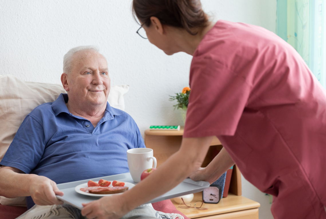 A nurse is serving food to an elderly man in a hospital bed.