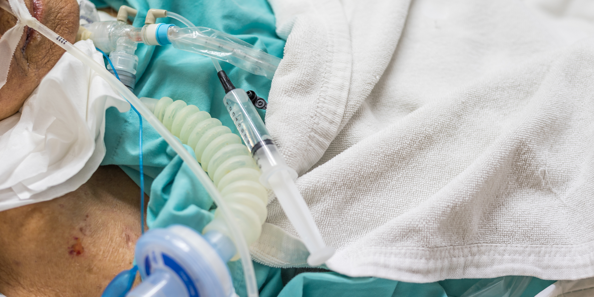 A man is laying in a hospital bed with an oxygen mask on his face.