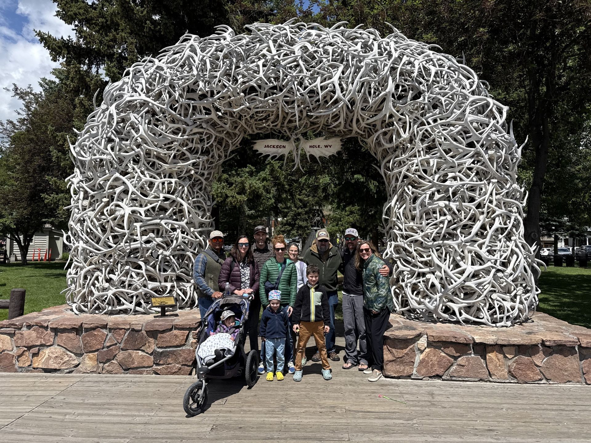 Group posing beneath a large arch made of white bones in a park, with two skulls above the opening.