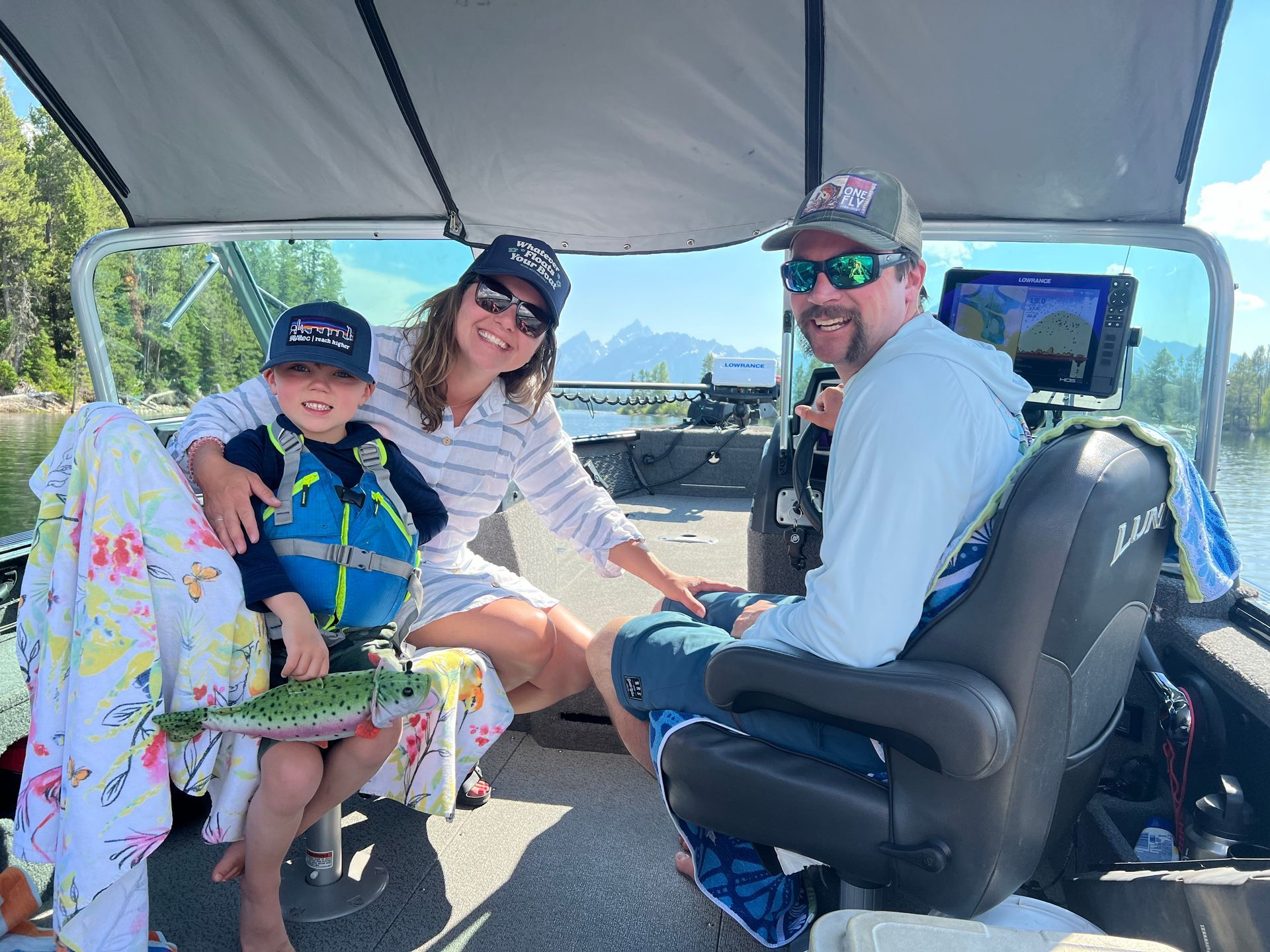 Three people smiling in a golf cart under a canopy, with mountains and trees in the background.